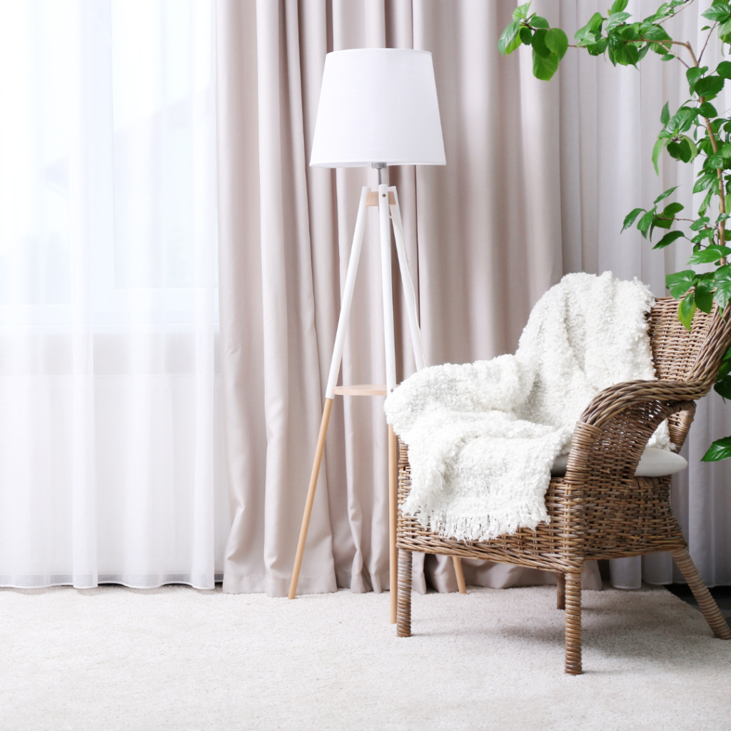 Coastal chair with cozy blanket, gauzy curtains with natural light and a modern, coastal lamp