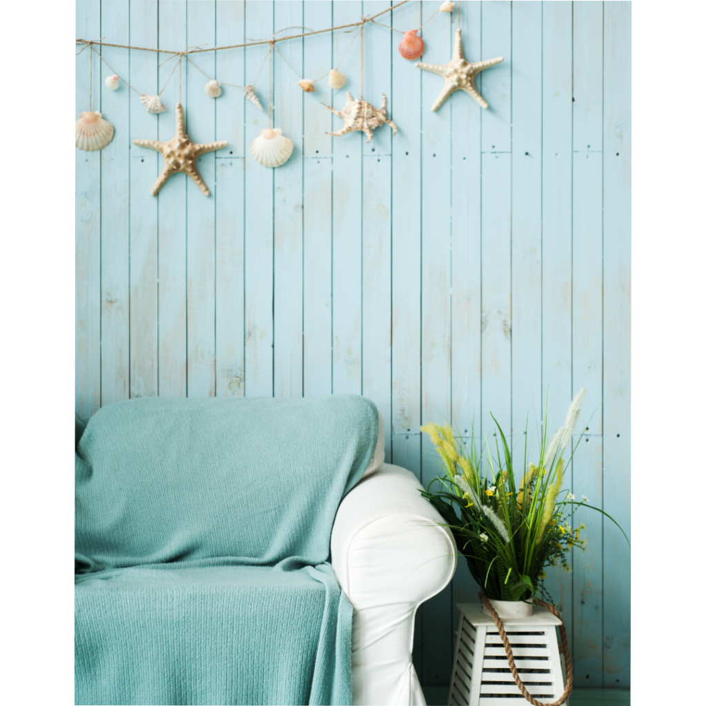 A linen couch with a coastal blanket and shell decorations. Wall painted to look like weathered wood.