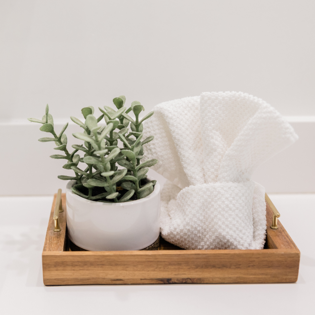 Natural wood tray with unique towel and greenery in ceramic pot for a coastal decor in your bathroom